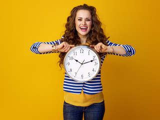smiling stylish woman against yellow background showing clock