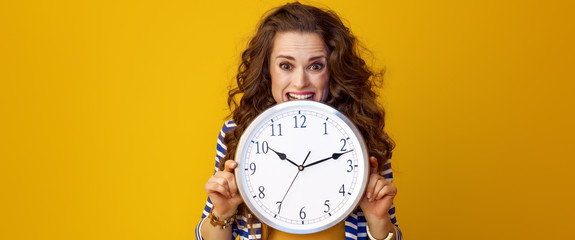 stressed trendy woman on yellow background biting clock