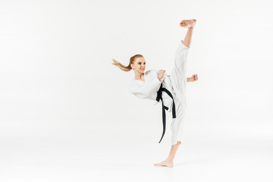 Female karate fighter with black belt performing kick isolated on white