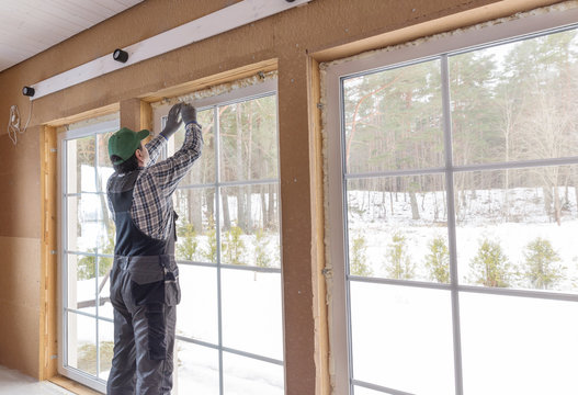Construction worker thermally insulating eco wooden frame house with wood fiber plates. Finishing the ceiling with a white wooden board. Latvia