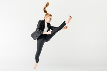 angry female karate fighter jumping and performing kick in suit isolated on grey