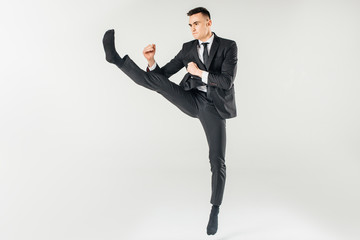 businessman jumping and performing kick in suit isolated on white