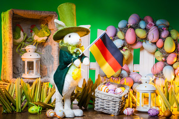 The Feast of Easter. Rabbit with colorful eggs. Easter holiday in Germany. A flag of Germany is holding an Easter bunny. Holidays in Germany