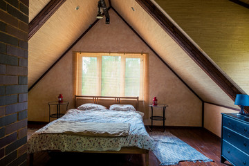 interior of a room with a bed on the top floor of a wooden house, under a roof