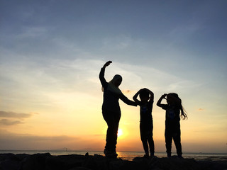 Fototapeta na wymiar Silhouette of young mother and sibling playing together at the beach on sunset 