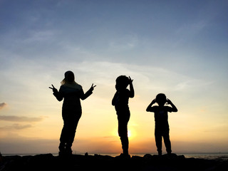 Silhouette of young mother and sibling playing together at the beach on sunset	