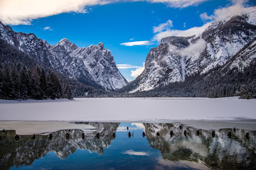 Reflection of mountain peaks in partly frozen lake, dolomites