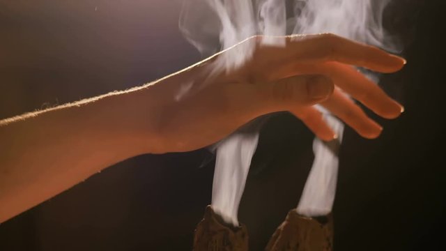 Smoke from incense rises through woman fingers. Warm romantic illumination, low key. Relaxation, meditative and aromatherapy concept