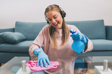 Happy woman with headphones listening music while cleaning house.