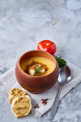 Clay pot of pumpkin soup on napkin over white textured background, close-up, selective focus, top view.