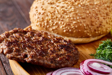 Yummy hamburger ingredients artistically organized on wooden plate, close-up, top view, selective focus