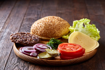 Yummy hamburger ingredients artistically organized on wooden plate, close-up, top view, selective focus