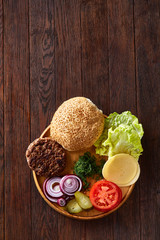 Yummy hamburger ingredients artistically organized on wooden plate, close-up, top view, selective focus