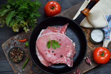 Raw piece meat of pork sprinkled with ground black pepper, salt and spices in a cast-iron frying pan on wooden background. Preparation for steak, roasting, stewing. Space for text.