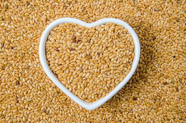 Background made of flax seeds with a heart shape bowl in the middle