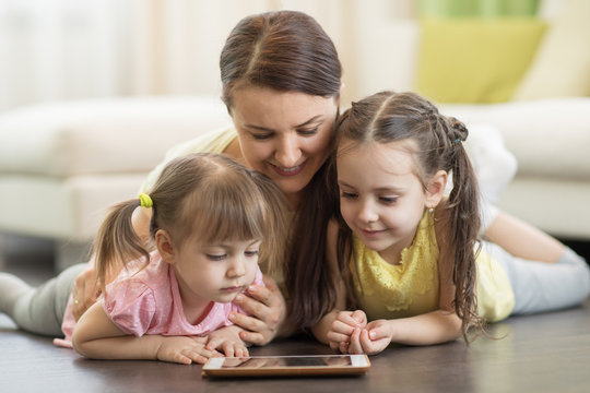 Mother with children daugters lying on floor and looking at tablet pc