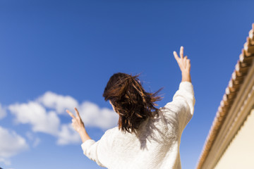 beautiful young woman making the victory symbol. View from the back. Windy daytime. Fun and lifestyle concept