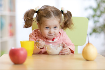 Funny little girl eating yogurt at home or daycare