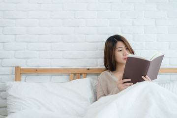 Lifestyle happy young Asian woman enjoying lying on the bed reading book pleasure in casual clothing at home. Relaxing lifestyle woman concept.