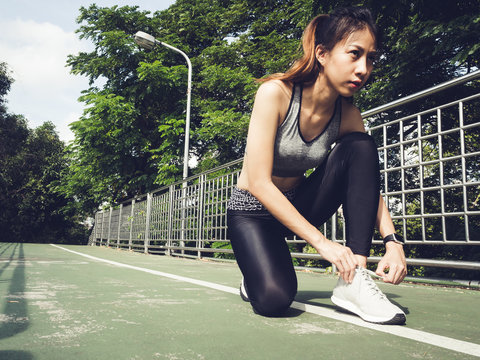 Close up of young woman lace up her shoe ready to workout on exercising in the park with warm light sunshine in morning. Young woman prepare for outdoor exercise in park. Outdoor exercise concept.