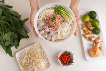 Female chef prepare traditional Vietnamese soup Pho bo with herbs, meat, rice noodles