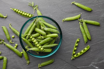 Fresh sweet peas pods in glass bowl on stone background, top view