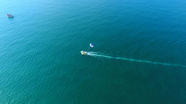 Man parasailing on parachute on black sea, Batumi, Georgia. Aerial camera shot of man flight on parachute towed by a motor boat