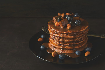 Stack of chocolate pancakes with icing, blueberry, almond, hazelnut and pieces of chocolate. Selective focus. Toned