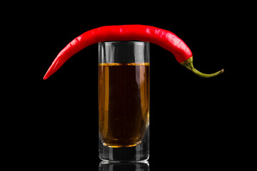 Glass with alcohol, top pod of bitter chili peppers, isolated on black
