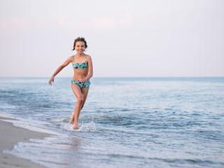 Happy smiling little girl running on sea shore at sandy beach during summer holiday. Action portrait of cute child outdoors.