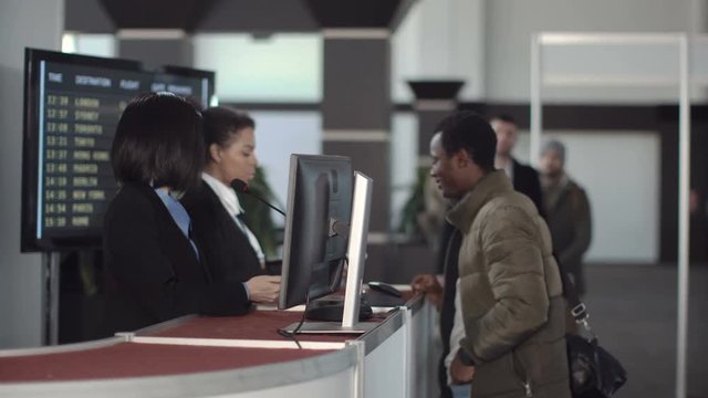 Two female airport security personnel checking identification at a check-in or boarding counter at the departure terminal holding the passports of two male passengers