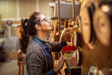 Side view of cheerful hardworking middle-aged industrial female engineer with eyeglasses choosing tools from shelves in the workshop.
