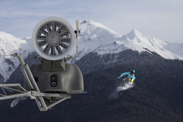 Naklejka na ściany i meble Snow cannon in the mountain ski resort and the flying snowboarder.
