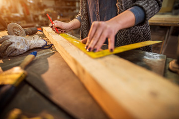 Close up view of hardworking professional carpenter woman hands working with a ruler and making marks on the wood at the table in the fabric workshop. - Powered by Adobe