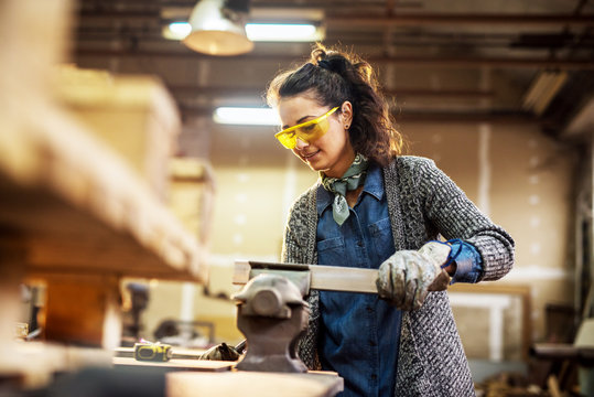 Professional charming cheerful carpenter woman preparing wood on steel vise in the fabric workshop.
