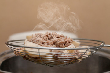pork chop in a basket that just boiled from hot soup in kitchen.selective focus.