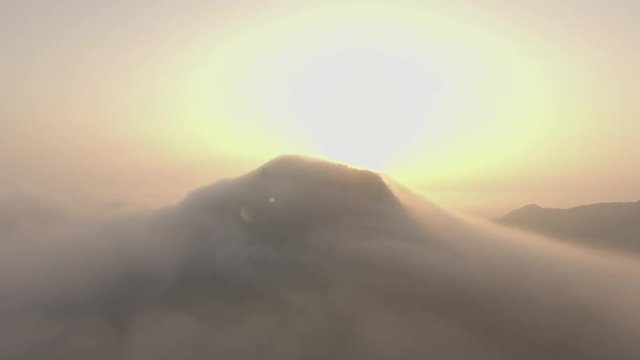 aerial shot of sunrise over the mountain peak covered by the cloud camera moving fast backward