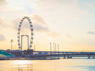 high and big ferris wheel at side of river of singapore with cloudy sky and sunrise background