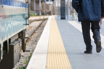 Fototapeta na wymiar Horizontal View of a Man Walking In a Railway Station Next to a Train on Blur Background.