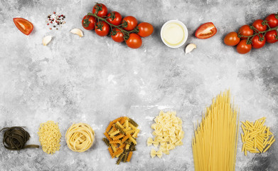 Various raw pasta and ingredients for cooking (tomatoes, olive oil, garlic) on gray background. Top view, copy space. Food background