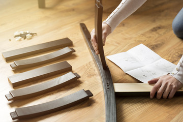 Assembly of wooden furniture, a woman putting together the wooden parts of the dining chair, using instruction. and a furniture screw and allen key.