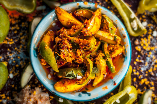 Close up of Aam ka achar or kari ka achar with all its ingredients and speiceis on a wooden surface in drak Gothic colors.