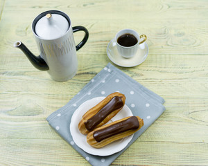 Eclairs and coffee on a wooden background.