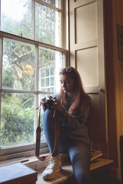 Woman reviewing pictures on retro camera near window