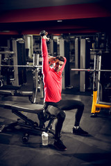 Fototapeta premium Inspiring young shape man doing exercise for triceps while sitting on the bench in the modern gym.