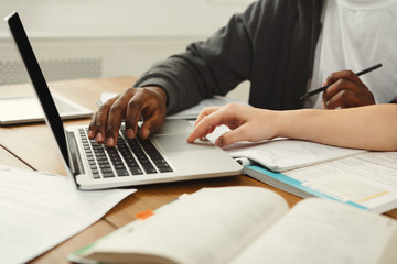 Male and female students at wooden table full of books