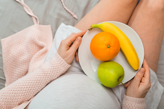 Pregnant woman eating fruits. Aerial close up view.