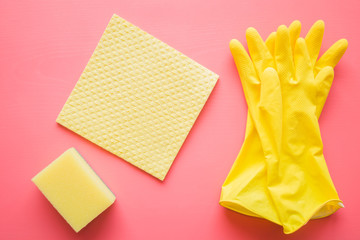Yellow rubber protective gloves with sponge and sponge cloth on the pink table for different...