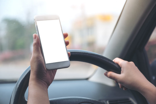 Mockup image of a hand holding and using white mobile phone with blank desktop screen while driving car on the road