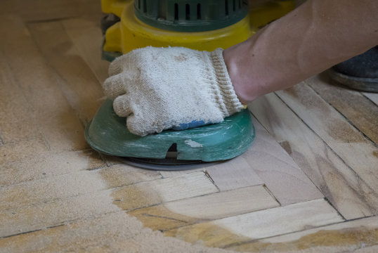 Worker polishing old wooden parquet floor with grinding machine